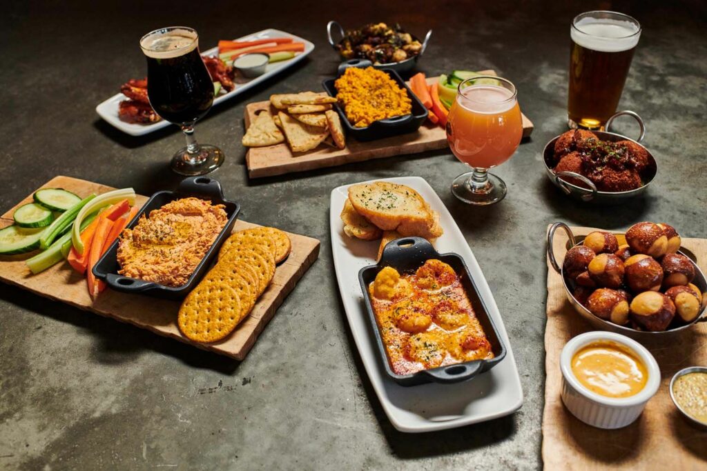 assortment of plates of food and glasses of beers from From the Earth Brewing